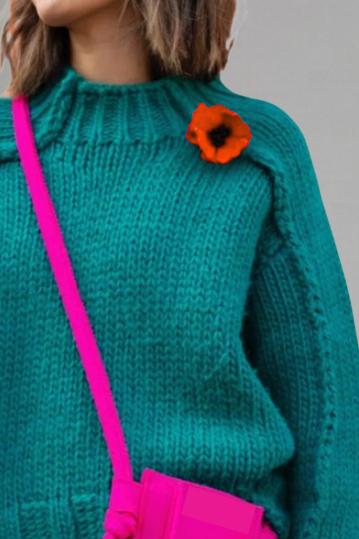 Person wearing a teal sweater with an wool red poppy brooch pin, holding a pink bag.