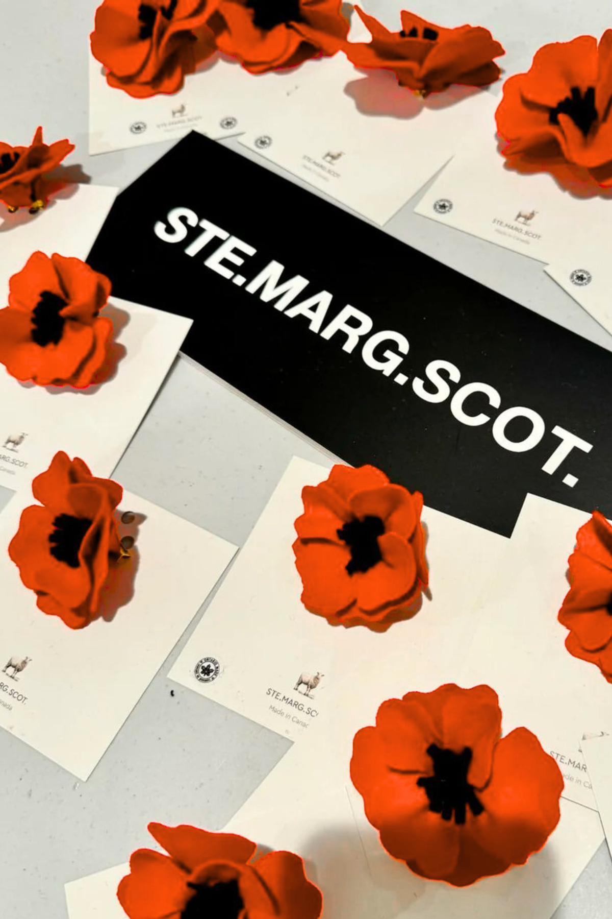 Red wool poppy brooches on white cards with 'ST. MARG. SCOT.' branding on a gray background